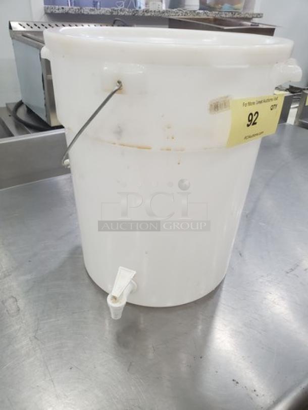 White 6-gallon beverage dispenser with spout, metal handle, label showing "92" indicating auction lot number, minor wear visible.