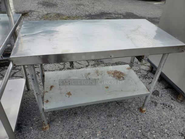 Stainless steel work table with missing drawer, shows visible wear. Features sturdy legs and lower shelf for storage.
