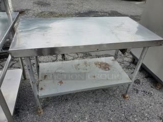 Stainless steel work table with missing drawer, shows visible wear. Features sturdy legs and lower shelf for storage.