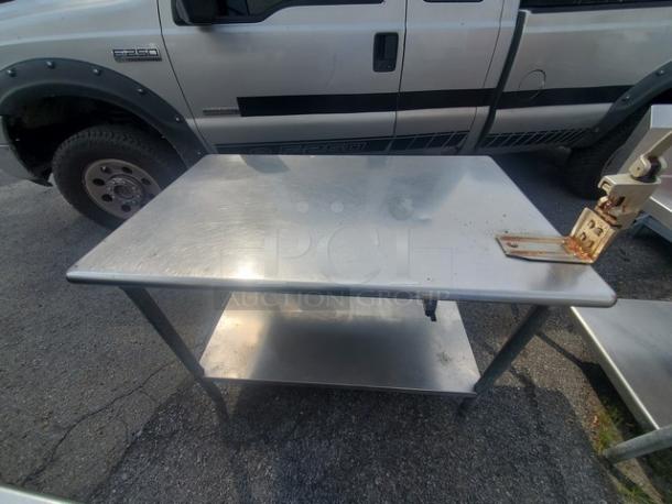Stainless steel work table with attached can opener, no drawer, scuff marks visible, lower shelf for storage, durable build.