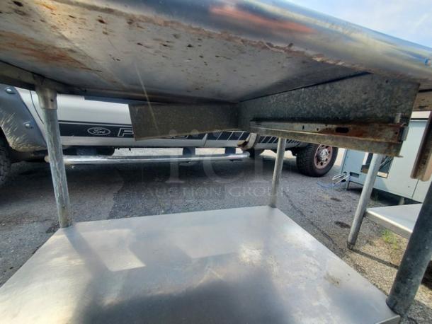 Stainless steel work table with attached can opener, visible wear and rust, no drawer. Suitable for industrial kitchens.
