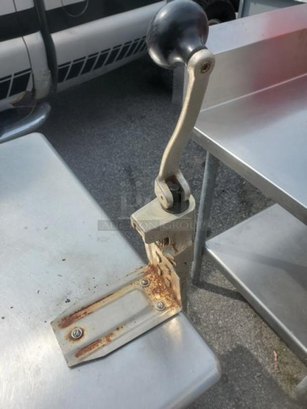 Stainless steel work table with can opener, no drawer. Shows signs of rust around can opener base. Ideal for commercial use.