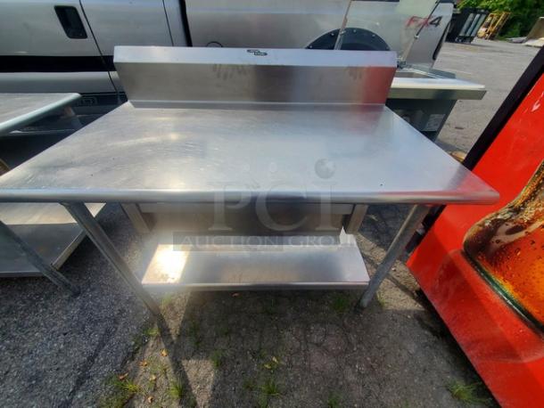 Stainless steel work table with drawer, features a backsplash, undershelf, and sturdy legs, in good condition.