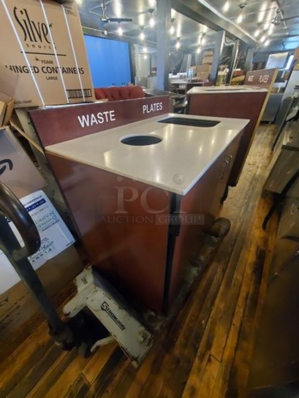 Commercial waste station with sections labeled "Waste" and "Plates." Features durable wood and metal design in used condition.