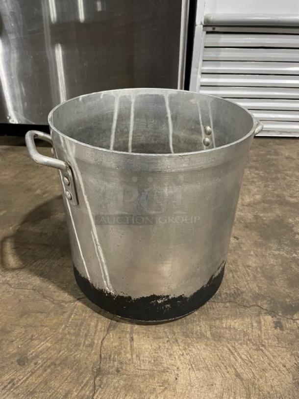 Commercial heavy-duty stock pot with handles, aluminum, visible wear on base, ideal for large-scale cooking.