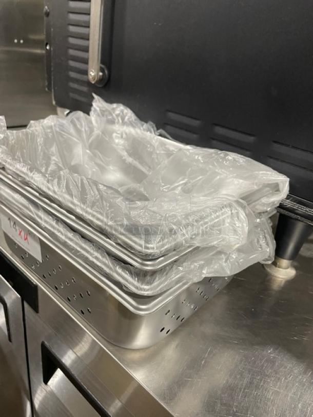 Stainless steel perforated hotel pans, Production 125th Model 880243, stacked with protective plastic. Appears new.