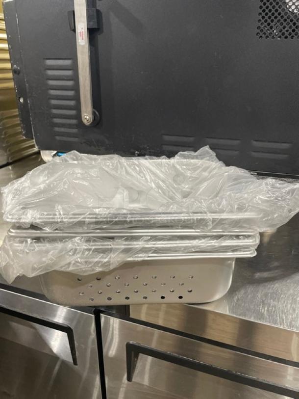 Production 125th stainless steel perforated hotel pans, model 880243. New condition, stacked, partially wrapped in plastic.