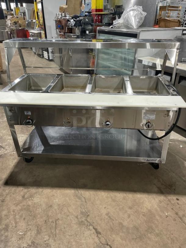 Duke Aero Hot Series EP304 stainless steel electric 4-well food table, with sneeze guard, cutting board, and undershelf.
