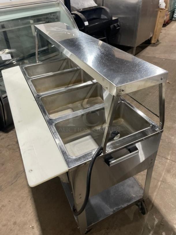Duke EP304 stainless steel electric 4-well hot food table with sneeze guard, cutting board, undershelf, and casters.