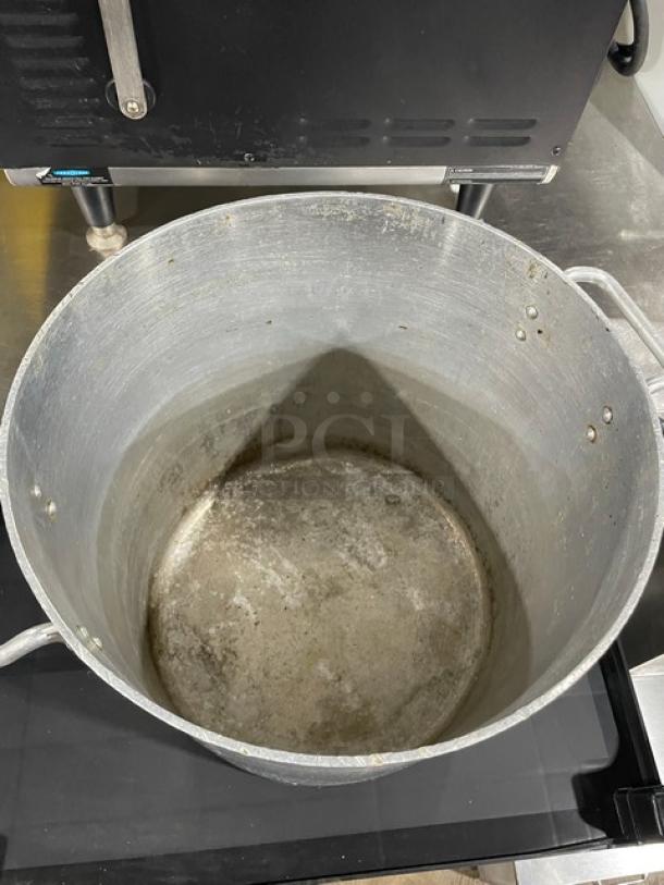 Commercial heavy-duty aluminum stock pot with handles, showing wear and discoloration but structurally intact.