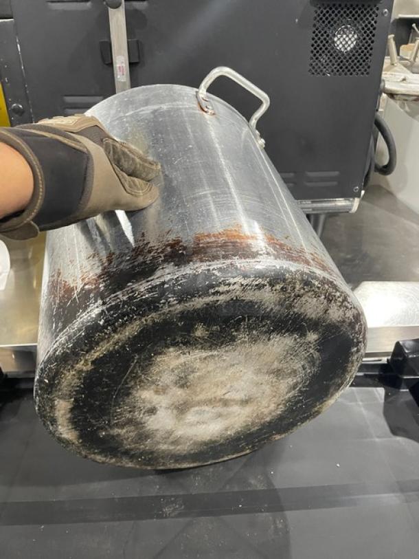 Commercial heavy-duty stock pot with handles, used condition. Visible scratches and wear on surface. Suitable for large-scale cooking.