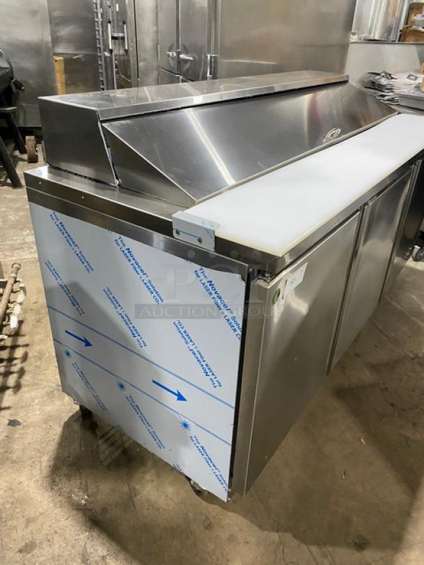 Stainless steel Asber APTS-72-18-HC 3-door refrigerated prep table, cutting board, wire racks, food pans, on casters.