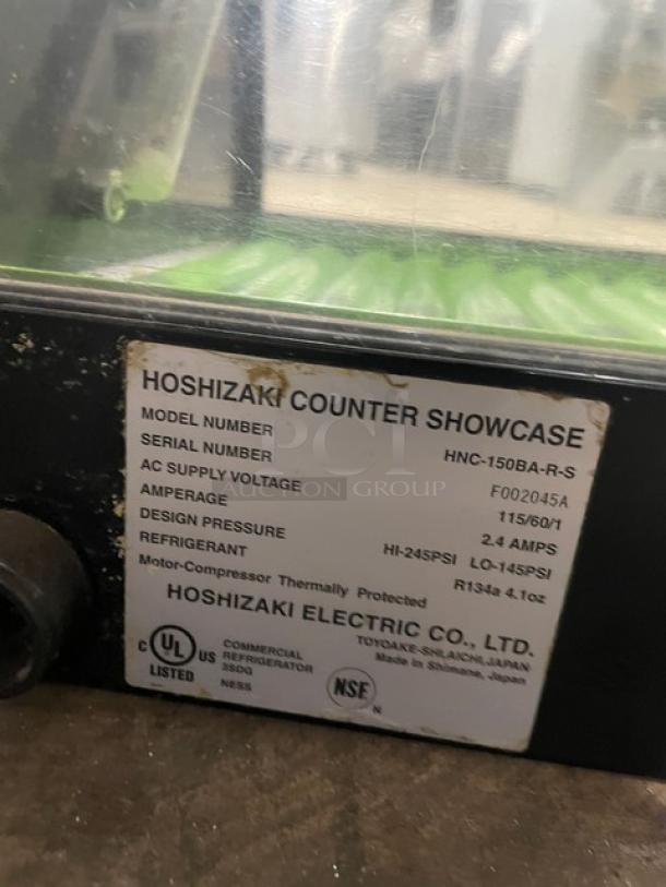 Hoshizaki stainless steel refrigerated sushi display case, model HNC-150BA-R-S, with rear sliding doors; tag shows 115V, 2.4A.