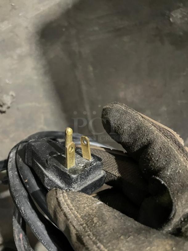 Close-up of a power plug with a glove holding it, part of the True Commercial Black Double Glass Door Freezer, model GDM43FHCTSL01.