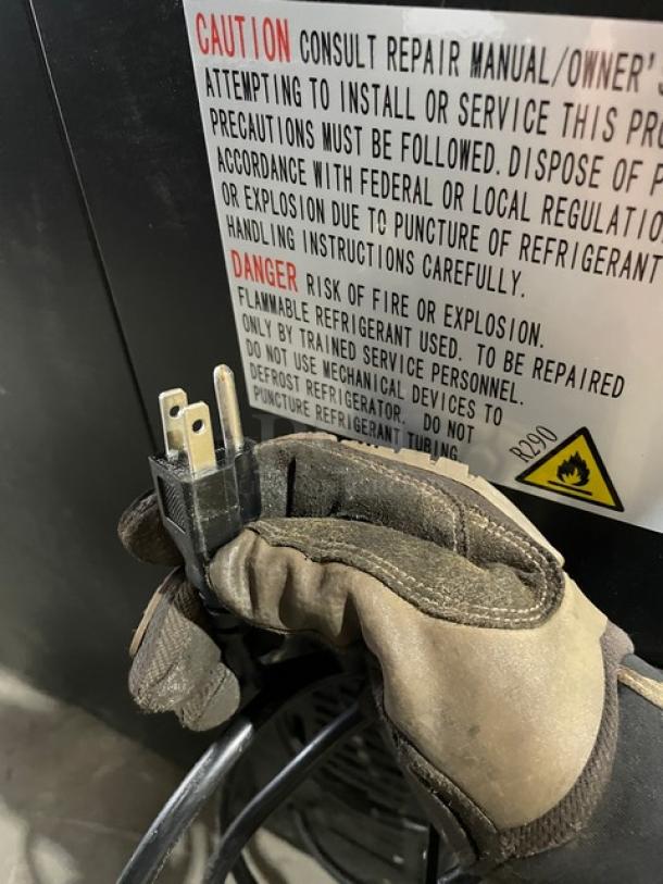 Gloved hand holding power cord against Kelvinator Commercial Refrigerator with warning label. Model KCBB48SB-HC, 115V.