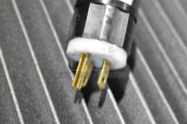 Close-up of a power plug with three prongs, possibly for the Lakeside bakery display rack, set on a textured surface.