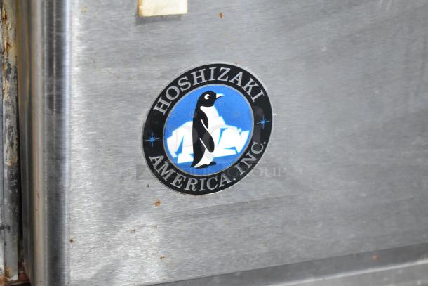 Hoshizaki KM-1340MRH stainless steel commercial ice head logo detail, features a black penguin on a blue background.