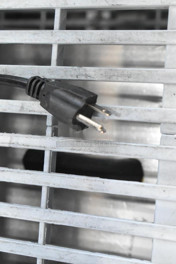 Close-up of a black power plug from a PrepLine MC12 commercial meat grinder, 110 volts, resting on a metal grate.