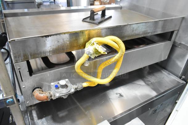 Cookline stainless steel gas countertop griddle, featuring flat top, control knobs, and yellow gas hose; shows signs of use.