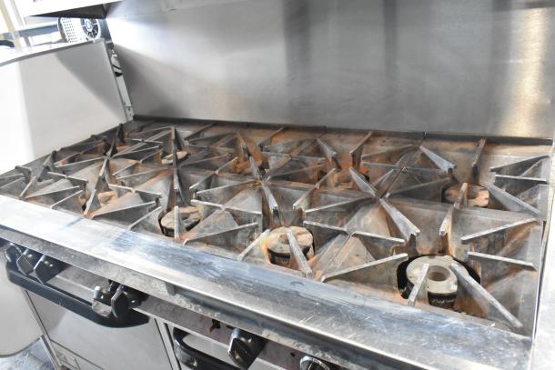 Southbend X460DD 10-burner stainless steel range with dual ovens, overshelf, and backsplash, showing moderate wear.