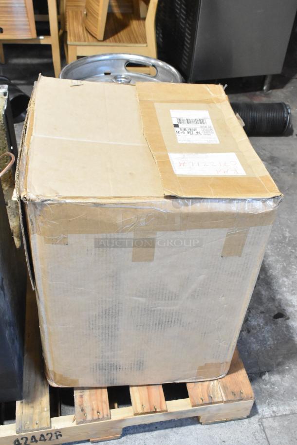 Brown cardboard box containing US Roaster Corp metal commercial roaster/smoker. Visible shipping label and handwritten note on top.