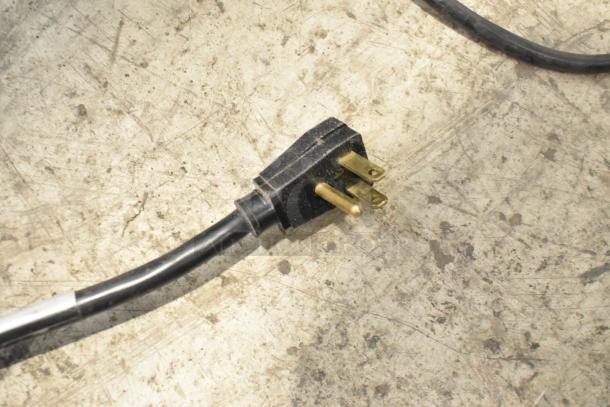Black electrical plug for True T-35 cooler, 115 volts, three-prong on a concrete floor.