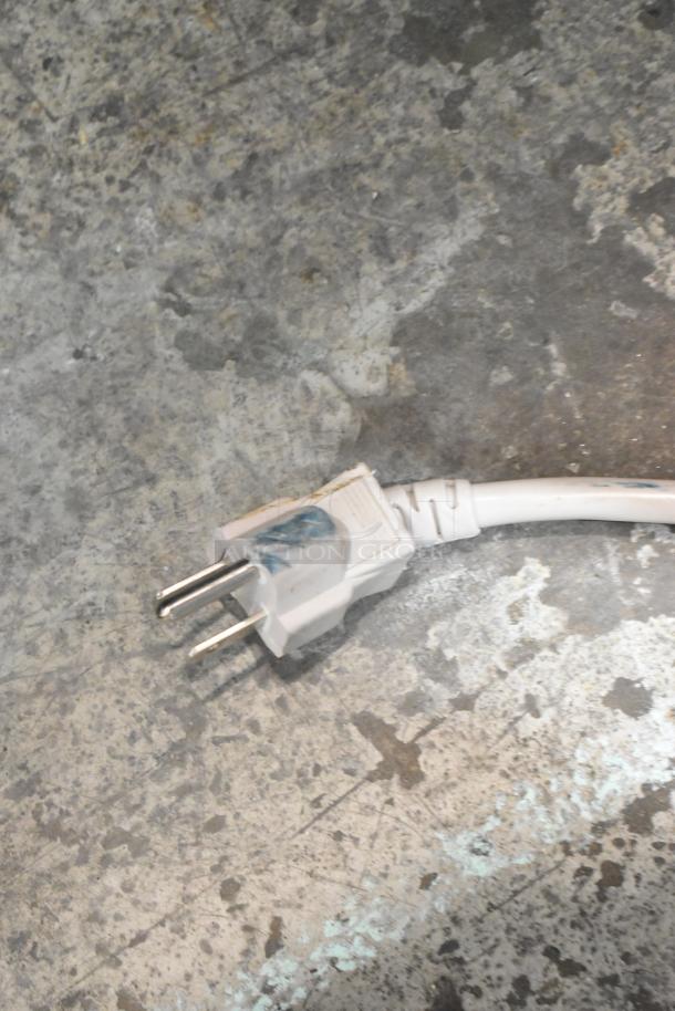 A white power plug on a textured, worn floor.