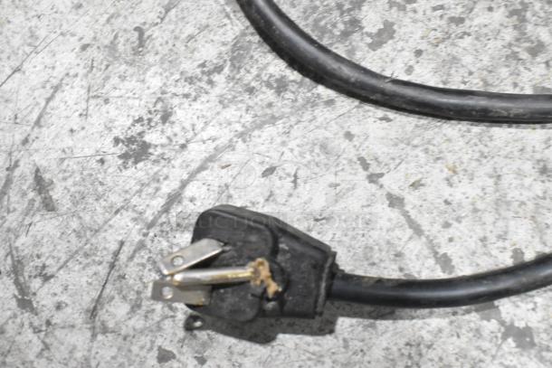Close-up of a black power cord with a three-prong plug on a concrete surface, part of Menumaster MDC182 microwave.