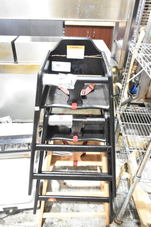 Three stacked wooden high chairs with black finish, red safety straps, and visible warning label. Auction item number 92.