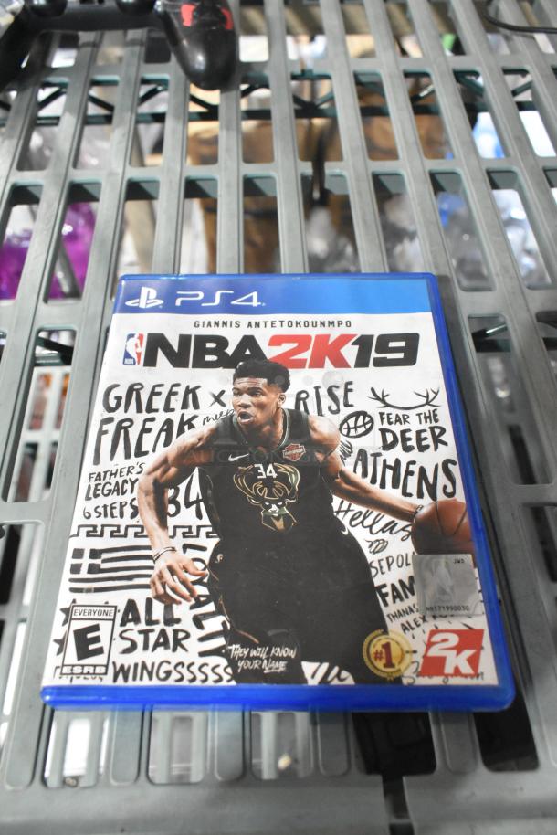 A set of four items on a shelf includes a PS4 NBA 2K19 game, headphones, a PlayStation controller, and earphones.