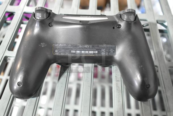 Sony PlayStation controller, model CUH-ZCT2U, black, visible wear, label with FCC and CE markings, on metallic grid.