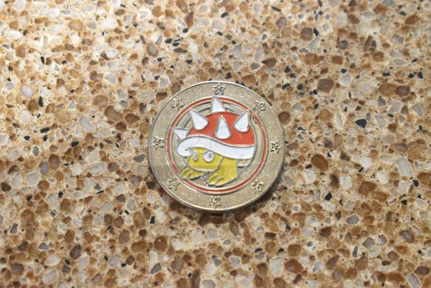 Coin featuring a Super Mario design with stars on the border on a speckled stone surface.
