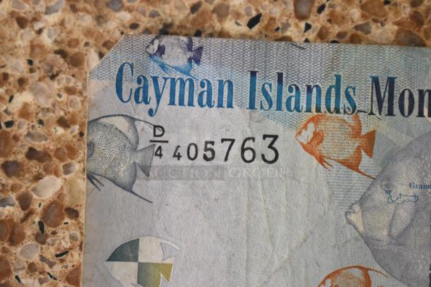 Close-up of a Cayman Islands Monetary Authority $1 note, serial number D/4 405763, vibrant fish design.