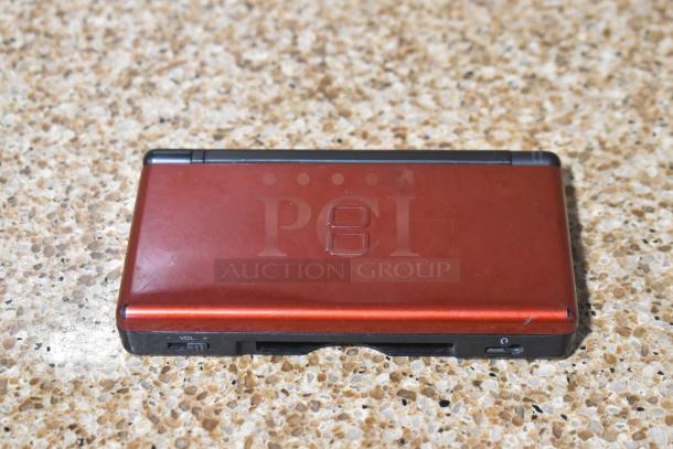 Red Nintendo DS game console with minor wear visible. Includes game and volume controls.