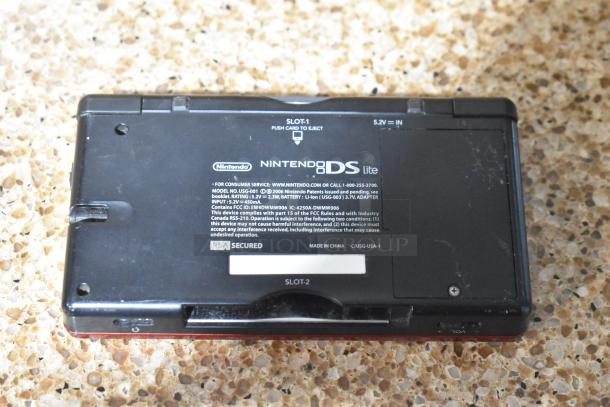 Back view of a Nintendo DS Lite console showing model and FCC markings. Includes slots for games. Some wear visible.