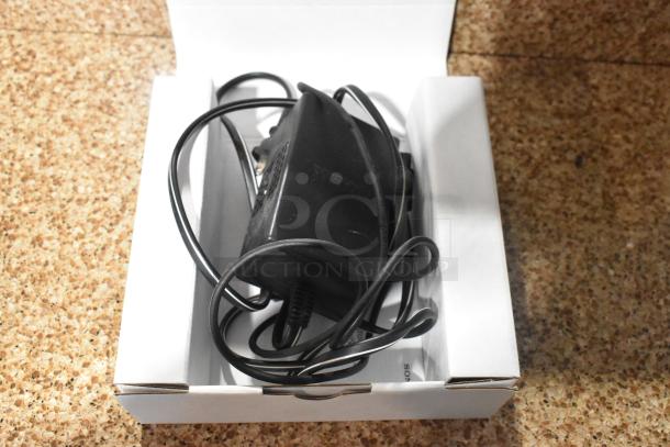 Box containing a black power adapter with tangled cord, placed on a white tray. No visible labels or markings.