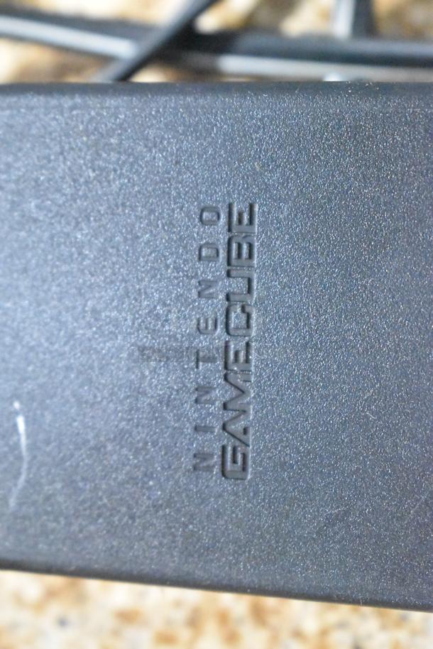 Close-up of a Nintendo GameCube adapter, showing the engraved logo. Part of a lot with six various gaming items.