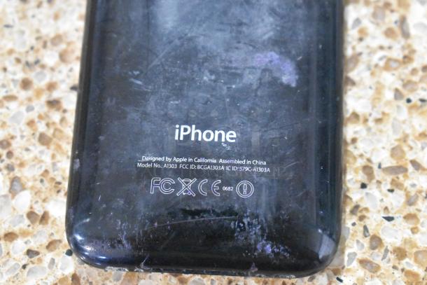 Close-up of an Apple iPhone Model A1303, showing wear, with label details including design and compliance markings.