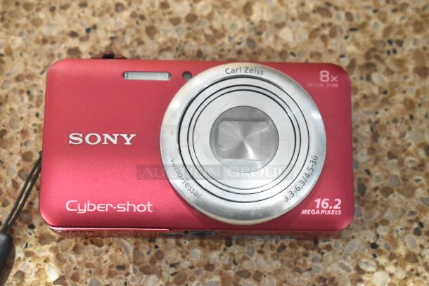 Red Sony Cyber-shot digital camera with Carl Zeiss lens, 8x optical zoom, and 16.2 megapixels, shown close-up.