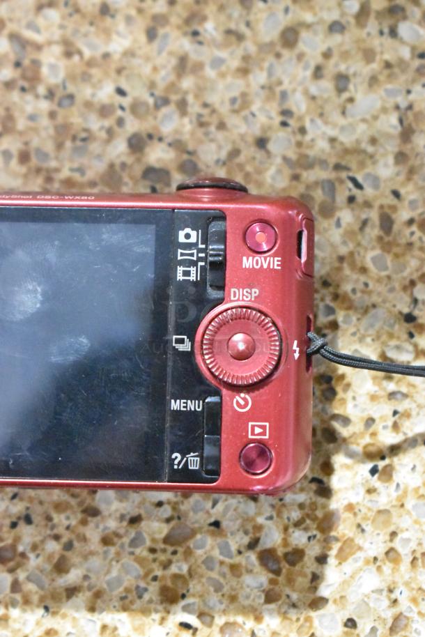 Red Sony Cyber-shot DSC-WX80 digital camera, rear view showing controls and screen, slight wear visible.