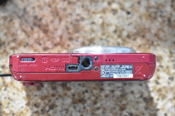 Sony Cyber-shot DSC-WX80 digital camera in red, HDMI, SD slot, slight wear, labeled with FCC ID. Part of auction set.