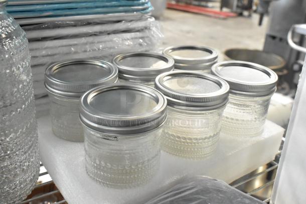 Nine new glass jars with metal lids, sitting on foam padding. Textured design, scratch and dent items.