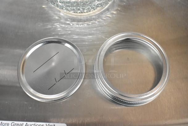 Brand new glass jar lid and ring set on metallic surface. Item is a part of a 9-piece scratch and dent deal.