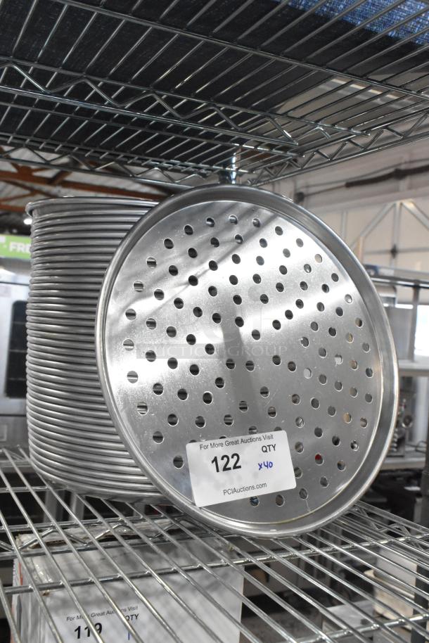 Stack of 40 brand new scratch and dent metal round perforated baking pans on a shelf. Auction label indicates lot 122.
