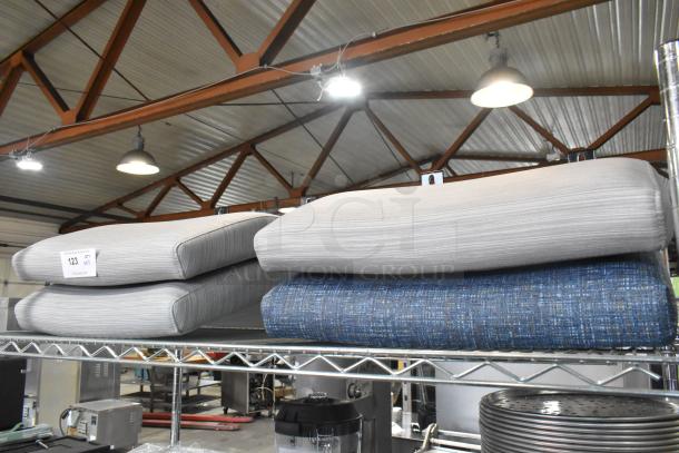 Four brand new seat cushions, blue and gray, labeled "Scratch and Dent," on a metal shelf in a warehouse setting.