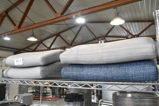 Four brand new seat cushions, blue and gray, labeled "Scratch and Dent," on a metal shelf in a warehouse setting.