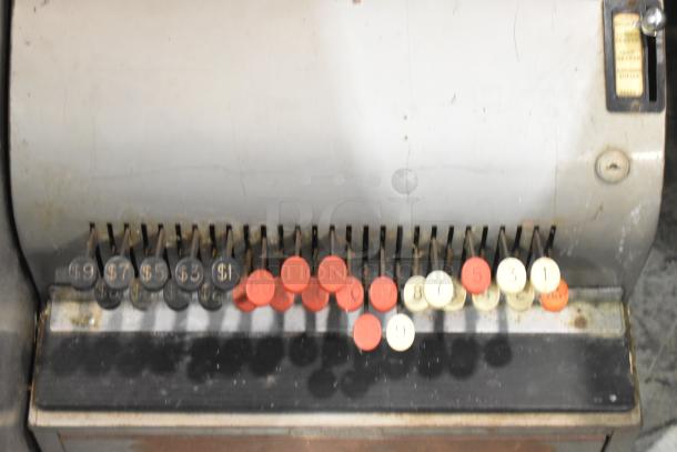 Vintage metal countertop cash register with multiple round buttons, showing wear and patina, ideal for collectors.