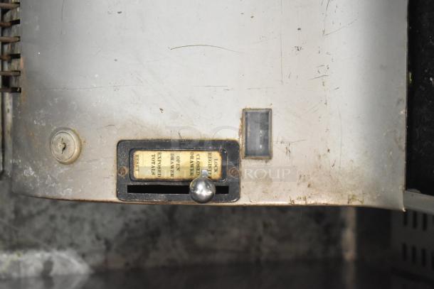 Vintage metal countertop cash register, featuring a visible reset knob and exposed totals display, shows signs of wear.