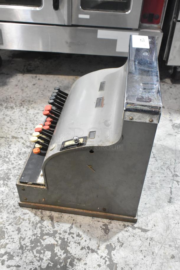 Vintage metal countertop cash register with red and white keys, showing moderate wear. Some surface rust visible.