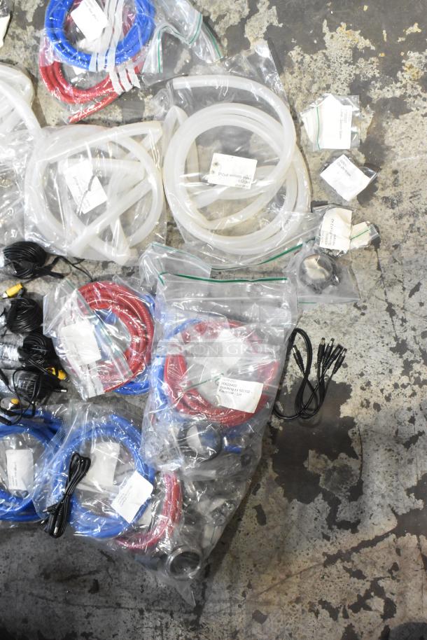 Lot of new scratch and dent items, including hoses and stacking kits in sealed bags with labels on concrete floor.